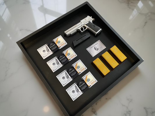 A shadowbox featuring a gun model, stacks of US dollars, and gleaming gold bars, all set in a sleek black display case atop a marble surface.