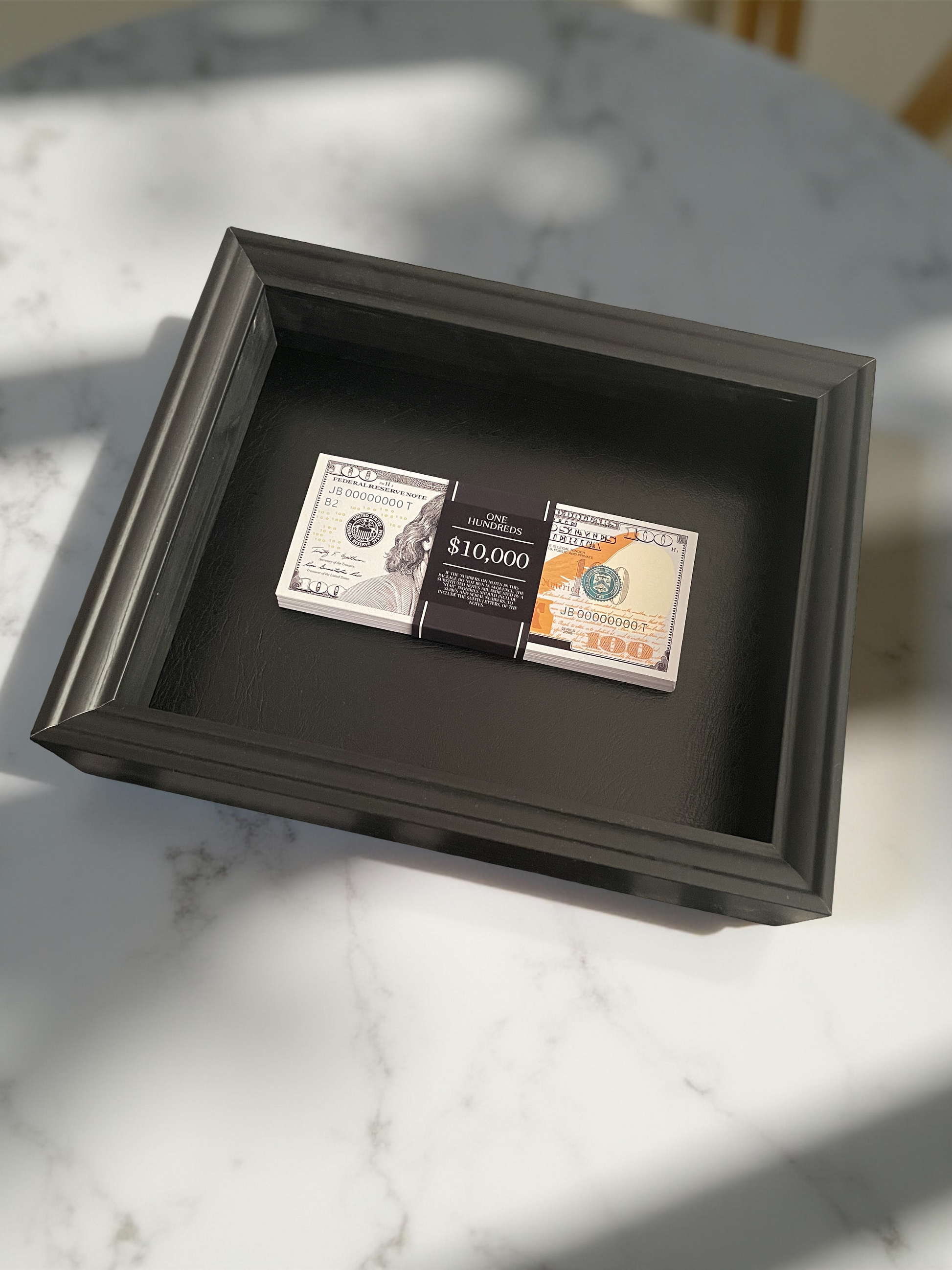 Black shadow box with US Dollar Stack on a marble surface.