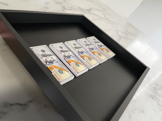 Five U.S. hundred-dollar bills arranged vertically in a black shadow box on a marble surface.