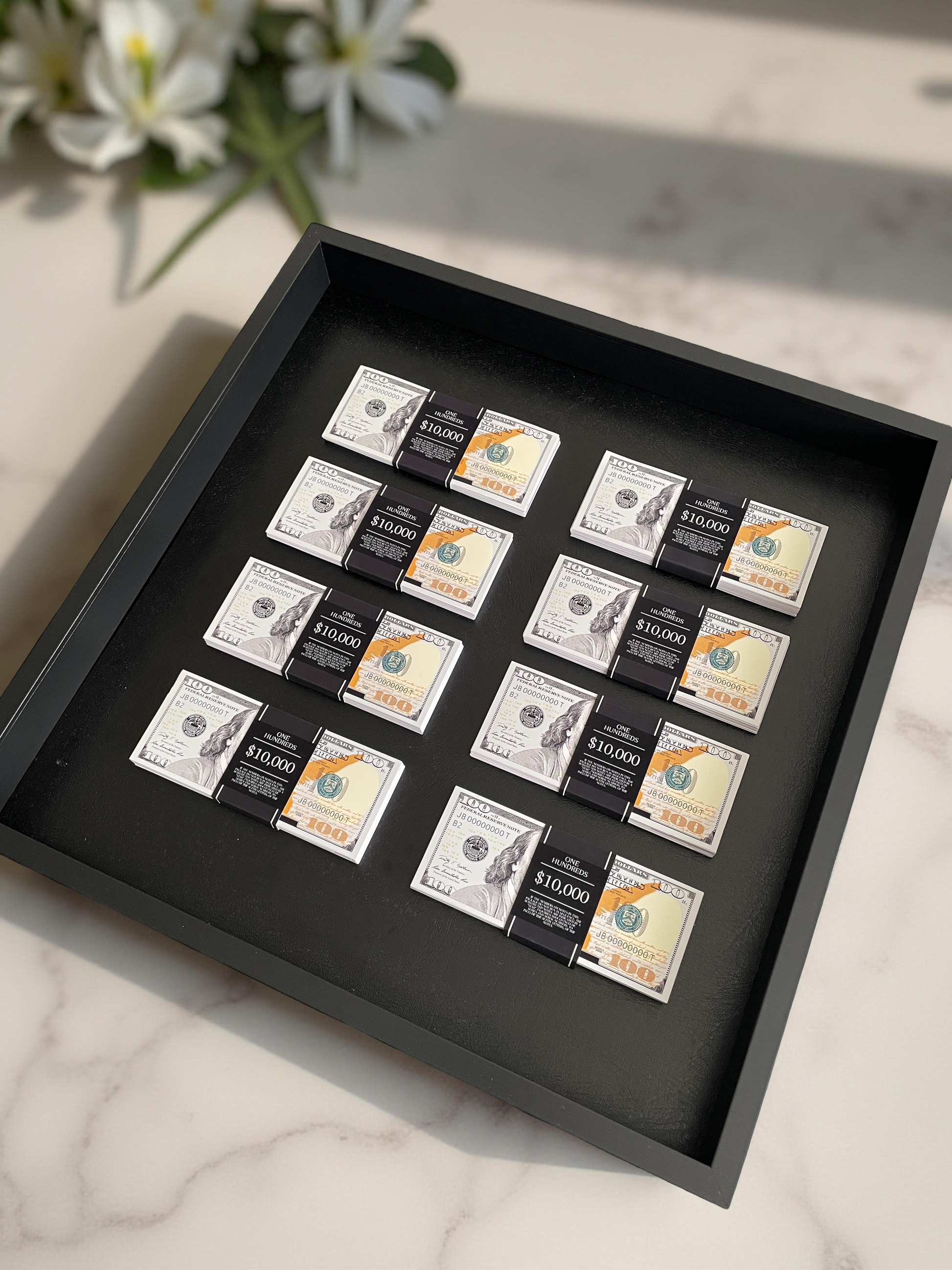 A collection of eight stacks of USD in a black shadowbox, placed on a marble surface.