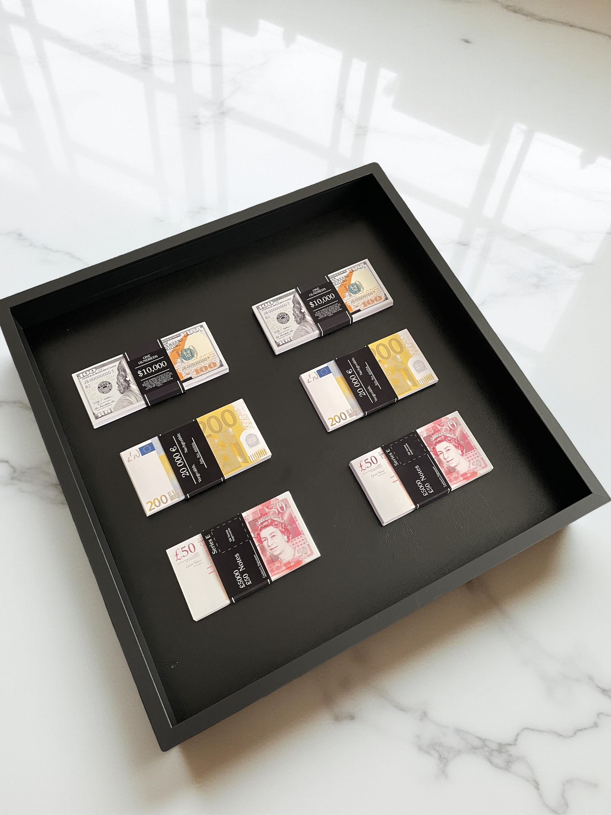 Stacks of USD, GBP, and EUR currencies artfully arranged in a black shadowbox, set against pristine white marble.