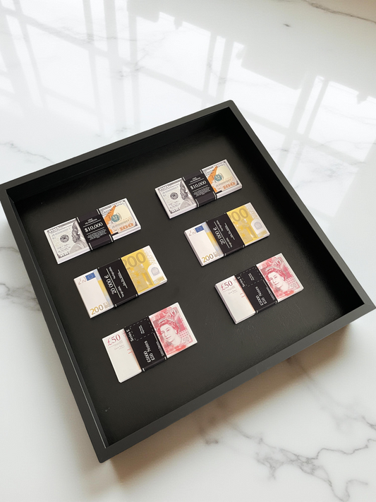 Stacks of USD, GBP, and EUR currencies artfully arranged in a black shadowbox, set against pristine white marble.