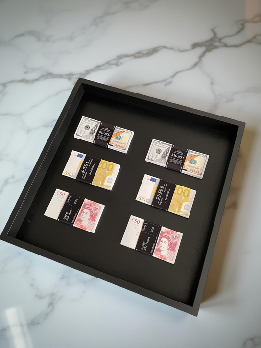 Stacks of USD, GBP, and EUR currencies artfully arranged in a black shadowbox, set against pristine white marble.